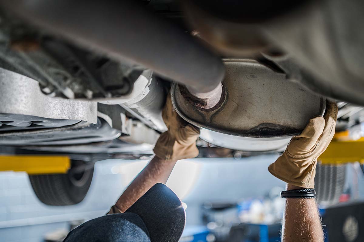 A mechanic inspecting a vehicle's exhaust system underneaht the car on an lift in a service garage.